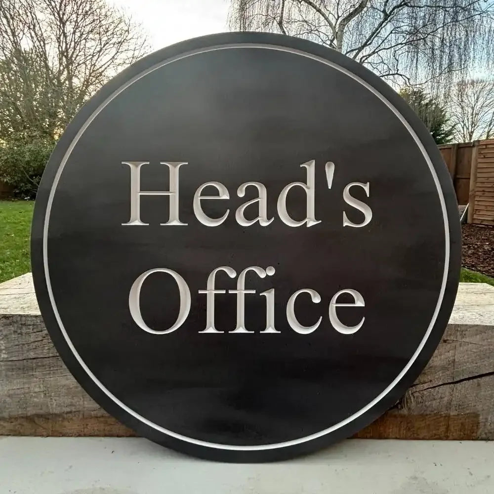 Round sign with 'Head's Office' text on a wooden surface outdoors
