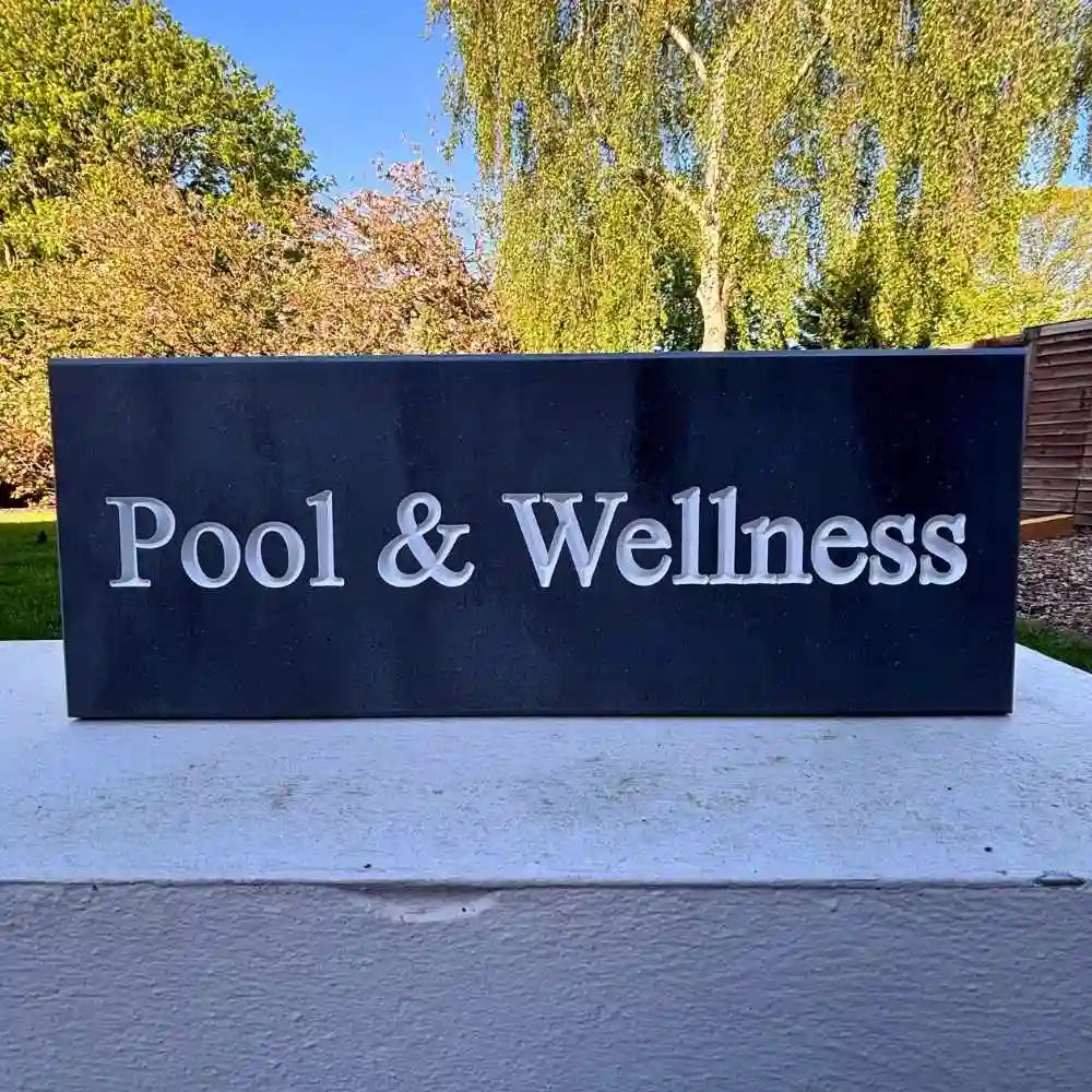 Sign with 'Pool & Wellness' text in an outdoor setting with trees and clear sky.