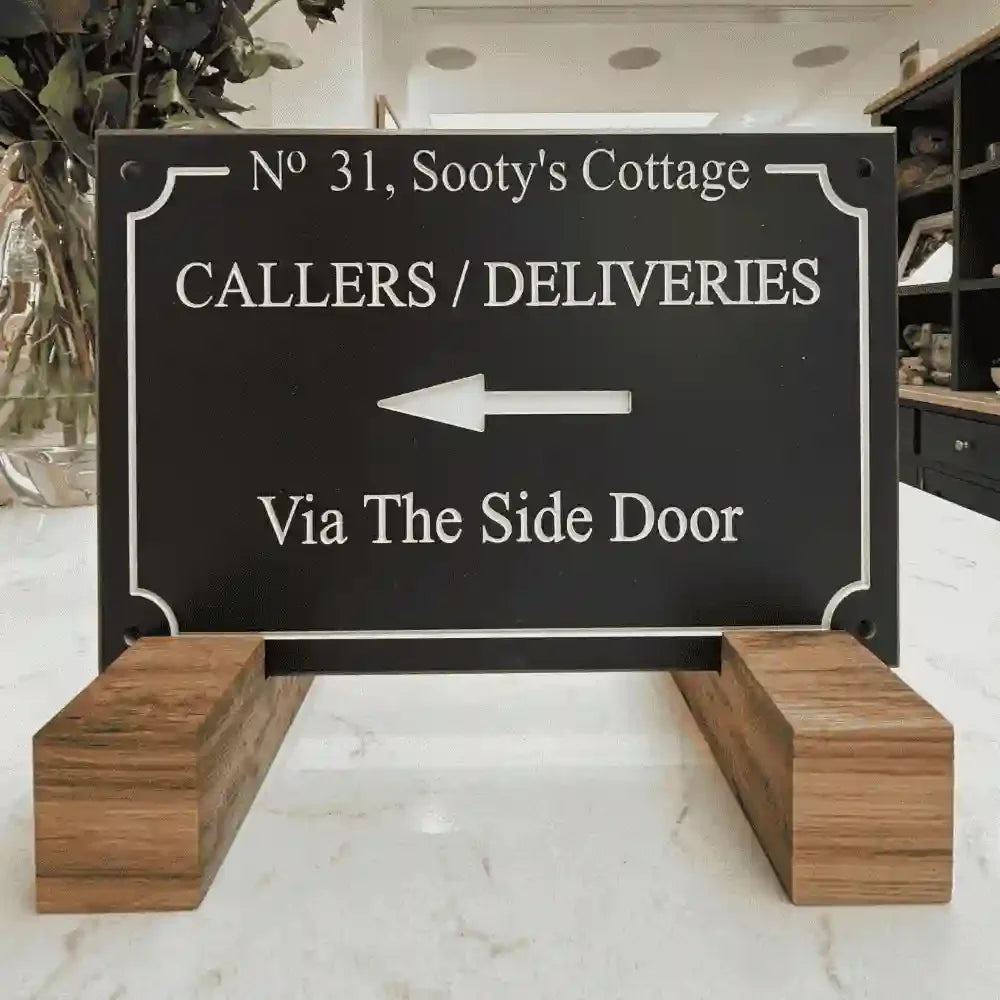 Decorative sign for callers and deliveries with an arrow pointing to the side door, placed on a wooden stand.