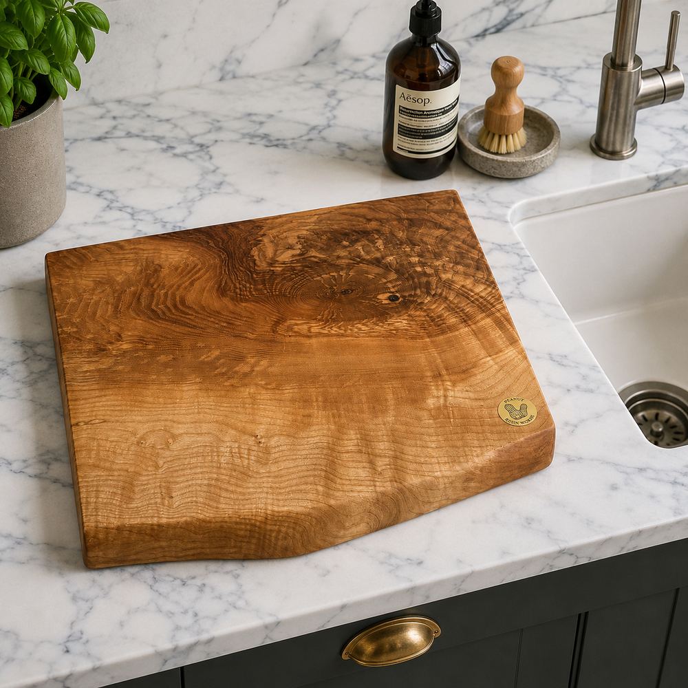 A large, polished live-edge wooden cutting board with dramatic grain patterns, resting on a white marble kitchen countertop next to a sink.