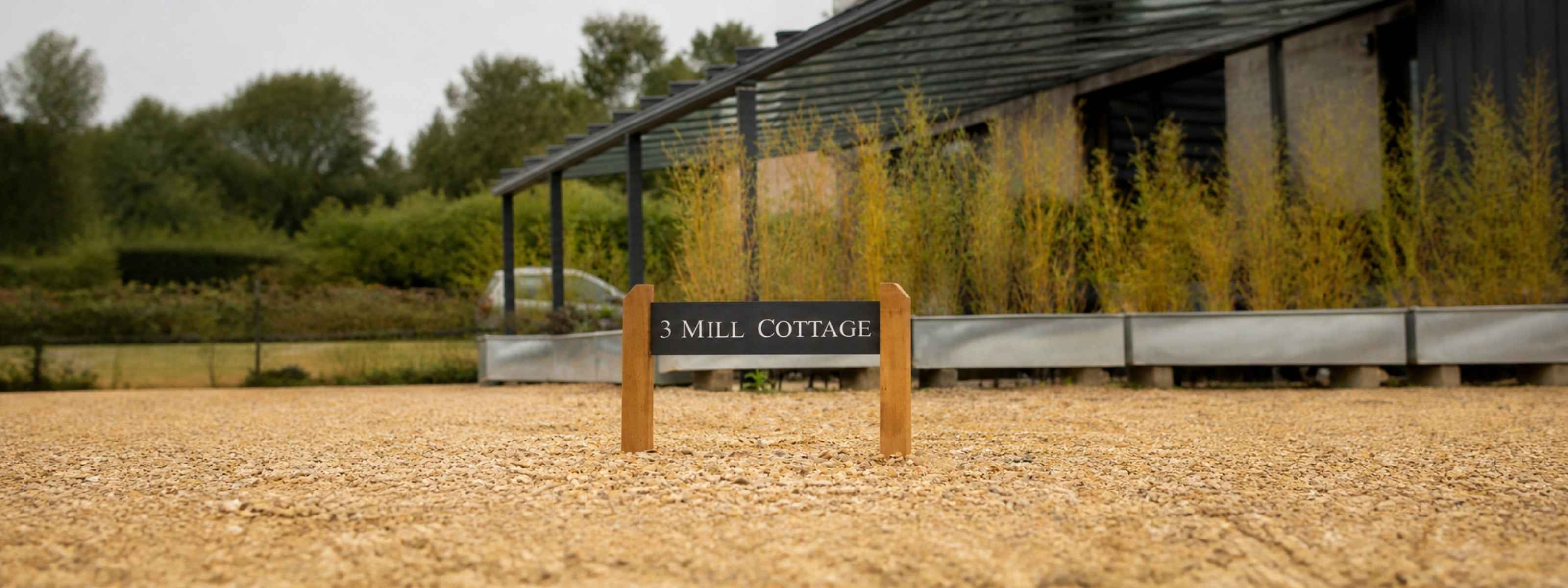 Wooden sign for 'Emill Cottage' in front of a building with greenery in the background