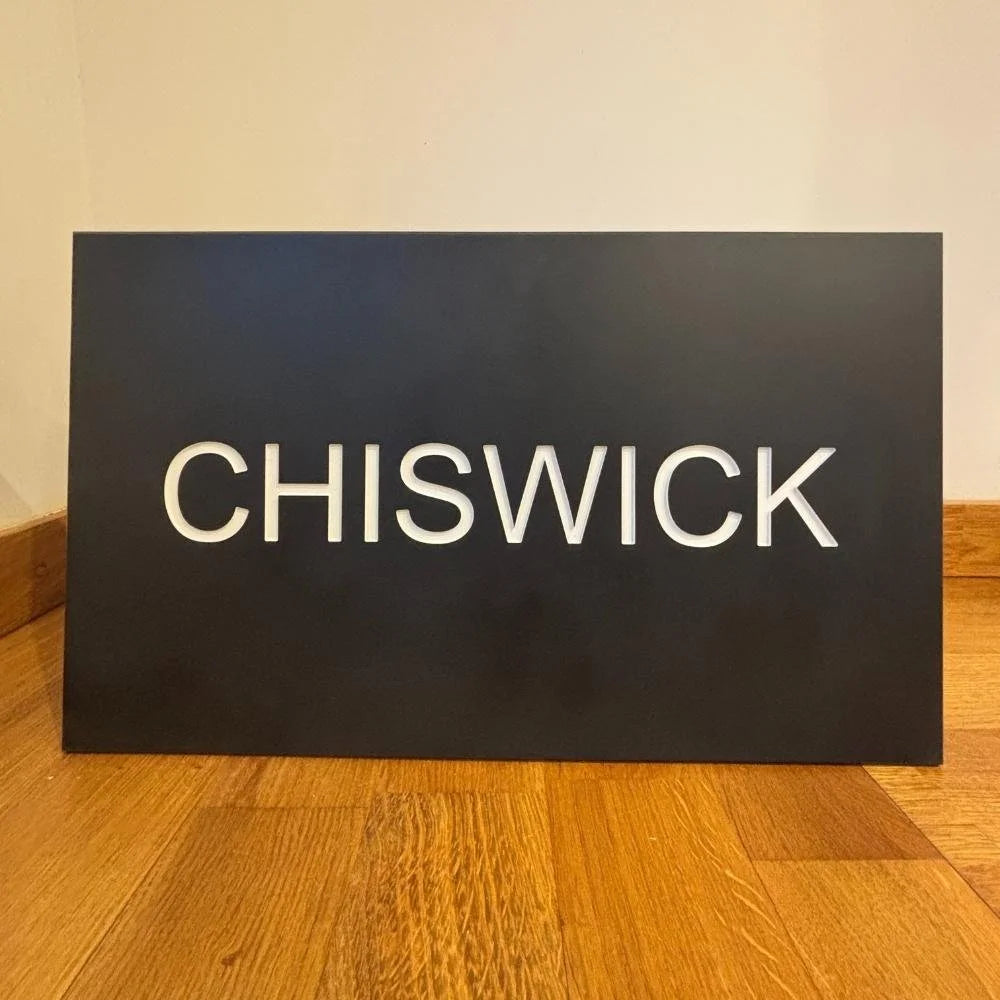 Black sign with 'CHISWICK' in white on a wooden floor.