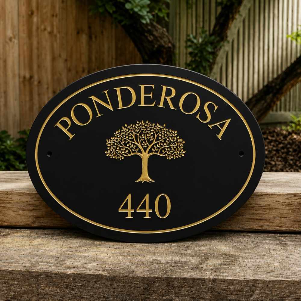 An oval black house number plaque with gold lettering reading 'PONDEROSA' and the number '440', plus a gold tree emblem in the center, photographed leaning on a wooden surface outdoors.