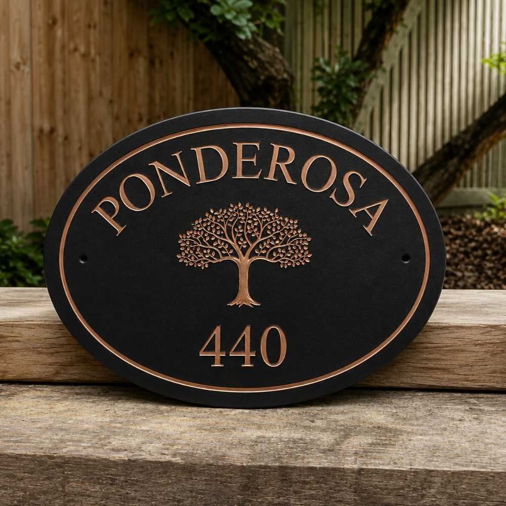 An oval charcoal house plaque with copper-toned lettering reading 'PONDEROSA' and the number '440', featuring a tree design in the center, displayed on a wooden surface outdoors.