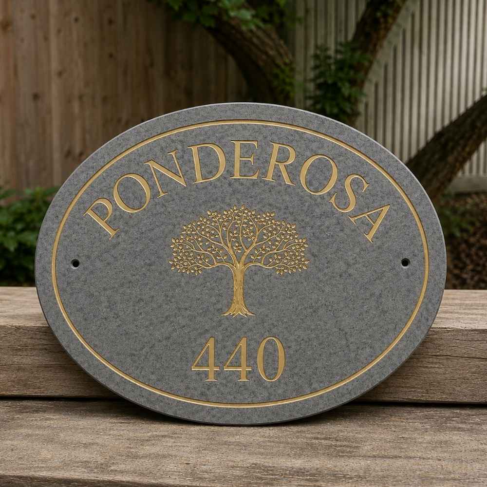 An oval charcoal granite house plaque with gold lettering reading 'PONDEROSA' and '440' around a gold tree emblem, displayed on a wooden surface outdoors.