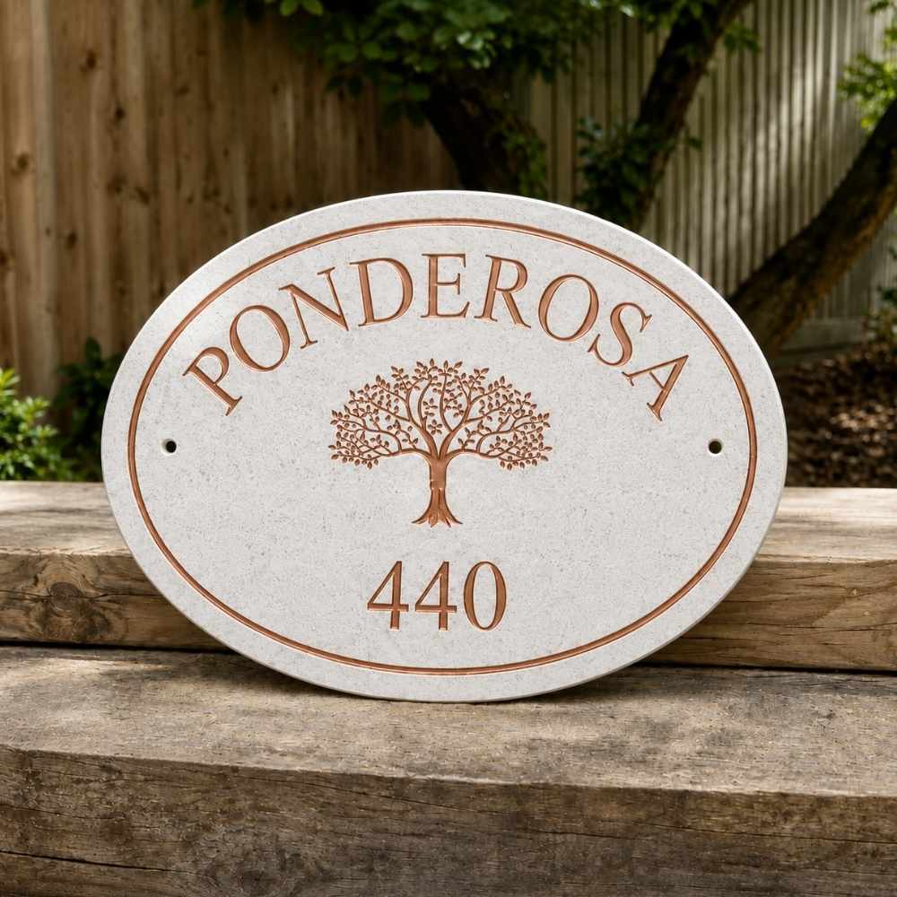 An oval quartz outdoor house plaque with a textured light beige stone-like finish, featuring the name 'PONDEROSA' and the number '440' in a copper-brown engraved style, along with a tree motif in the center. The plaque is displayed on a rustic wooden fence with a blurred wooden fence and garden foliage in the background.