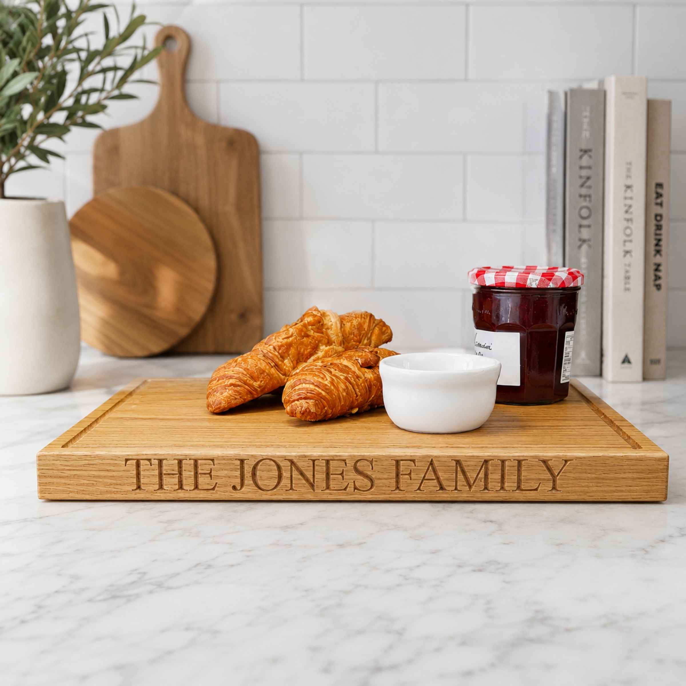 Wooden cutting board with 'The Jones Family' engraving, croissants, and jam on a kitchen counter.