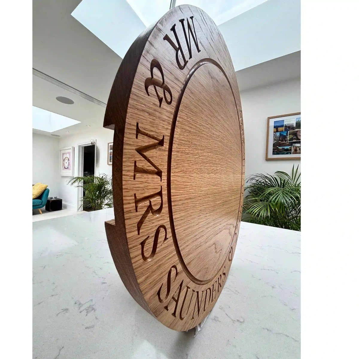 Wooden sign with 'MR & MRS SAUNDERS' engraved on it in a modern interior setting.