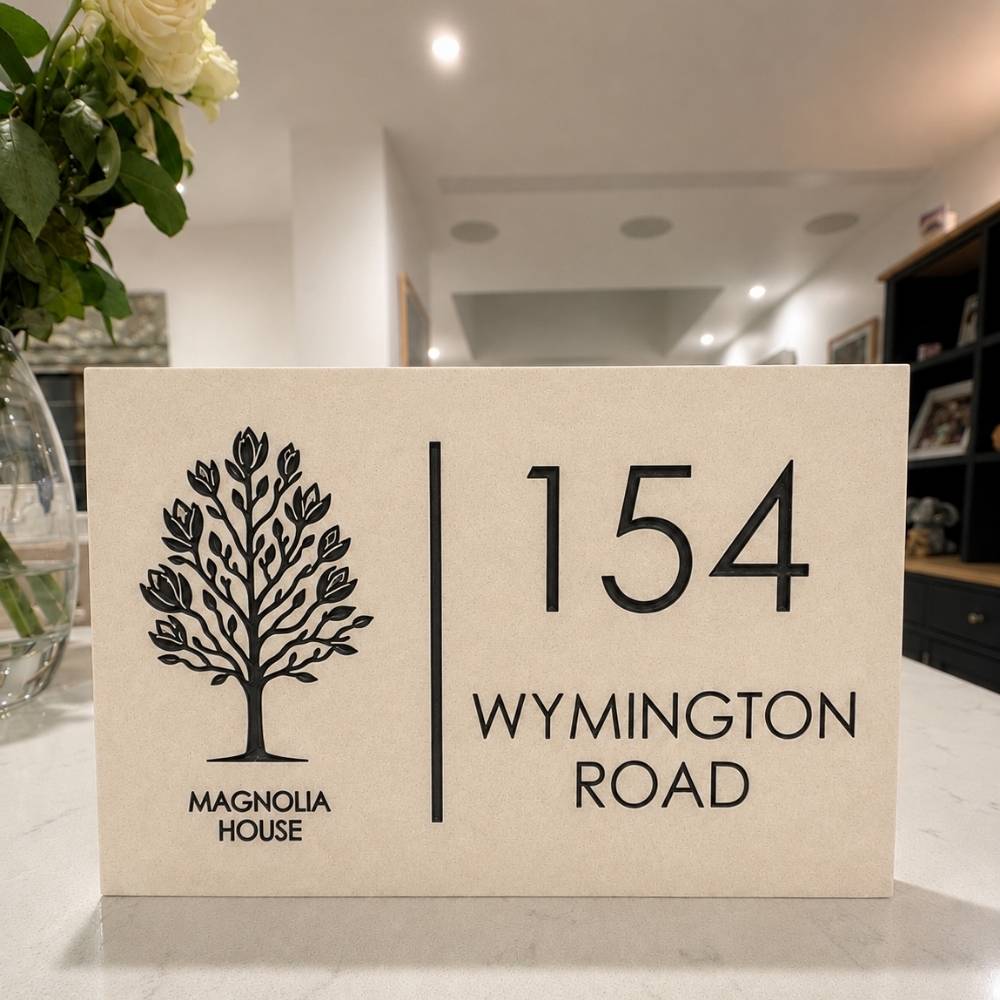 A quartz house sign for '154 Wymington Road, Magnolia House' with a black tree logo, displayed on a kitchen counter in a blurred home interior.