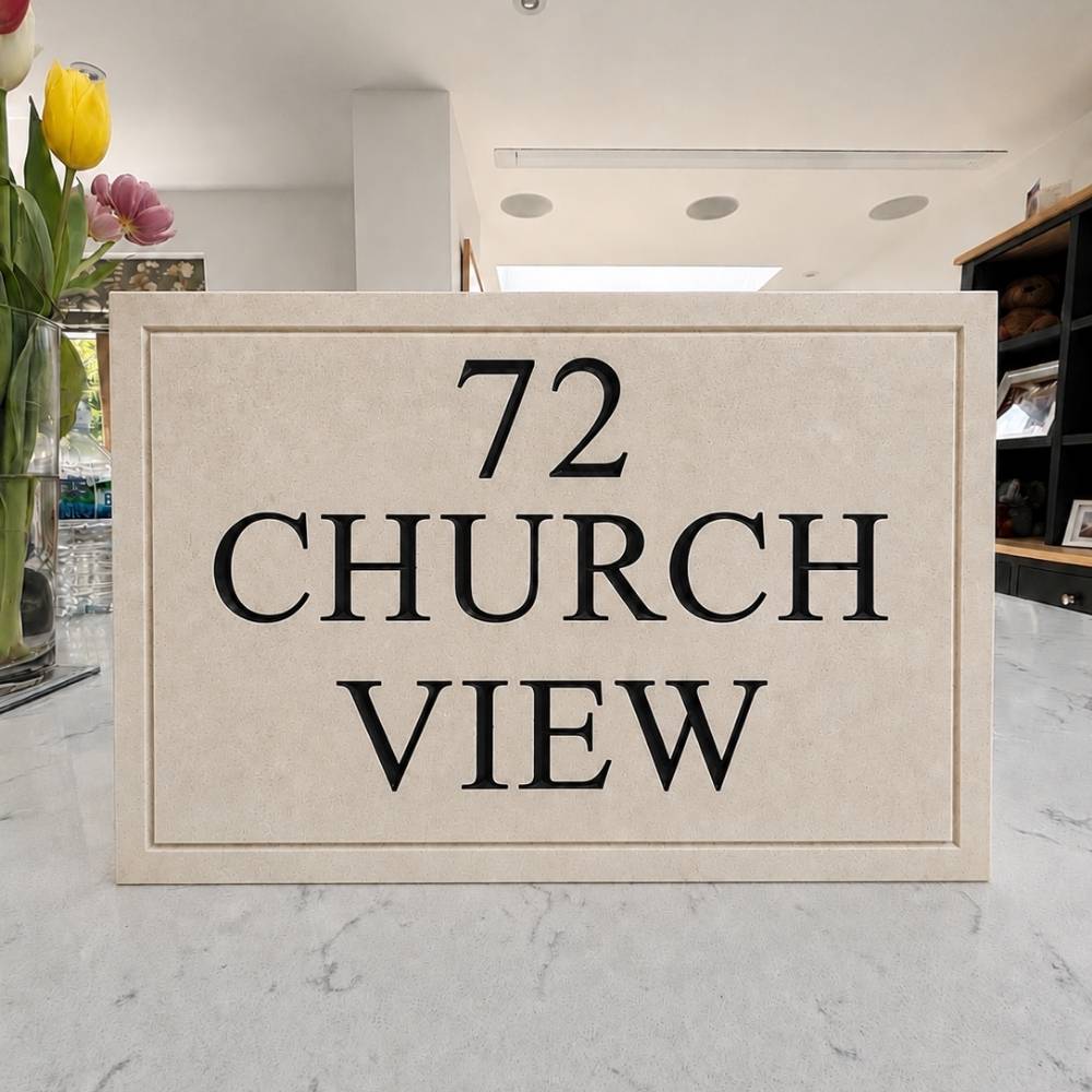 A rectangular limestone house number plaque reading '72 CHURCH VIEW' in black serif lettering, placed on a light marble countertop in a real indoor setting with flowers and shelving visible in the background.