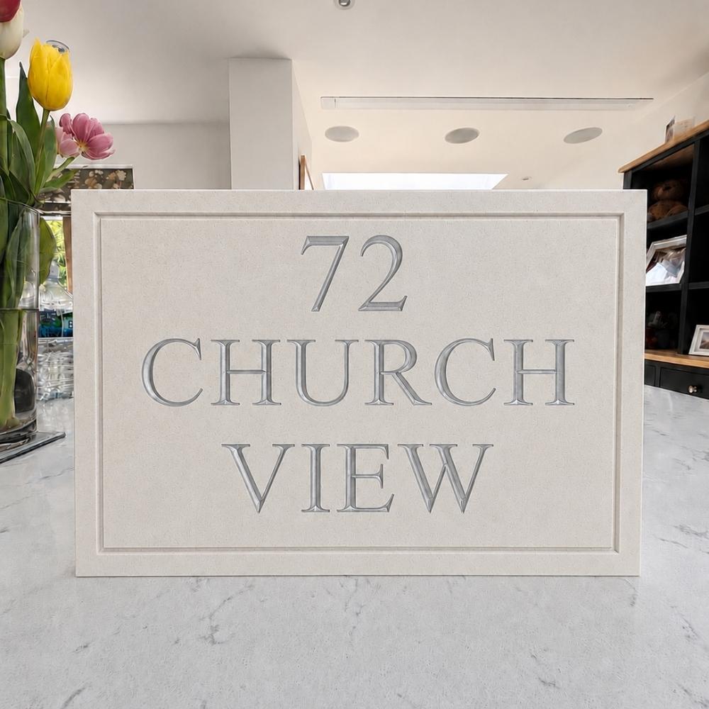 A rectangular quartz stone or concrete plaque with raised lettering that reads '72 CHURCH VIEW' in a matching light gray tone, displayed on a light marble countertop in a modern interior setting.