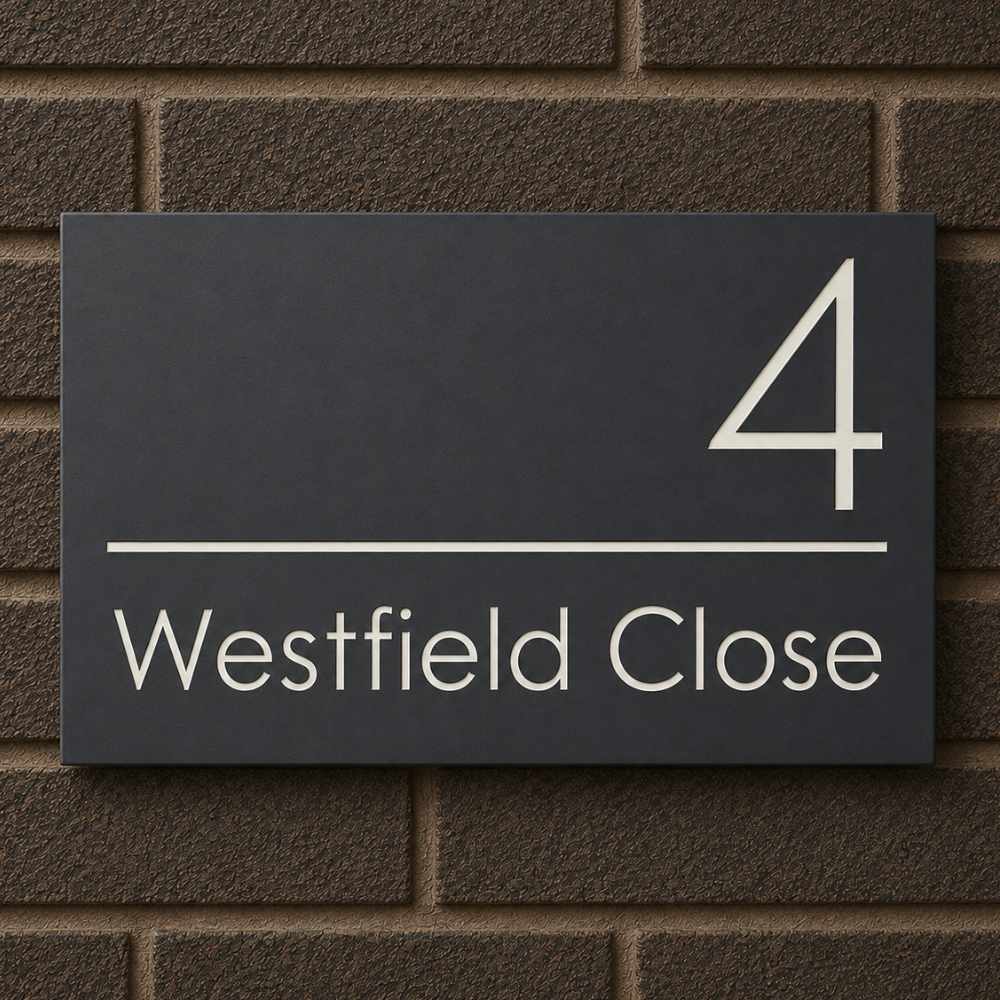 A rectangular dark house number sign mounted on a brown brick wall, with the number 4 and the text 'Westfield Close' in light gray.late