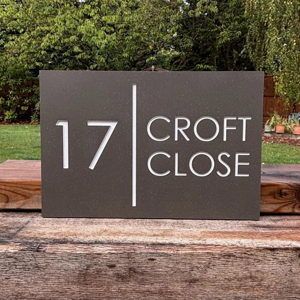 A mink House number sign '17 Croft Close' on a wooden surface with greenery in the background