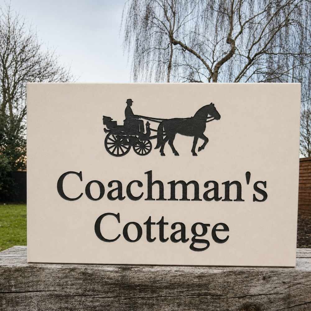 A rectangular limestone sign with a black silhouette of a horse-drawn carriage and the words 'Coachman's Cottage' in black serif lettering, displayed outdoors on a weathered wooden surface with trees and sky in the background.