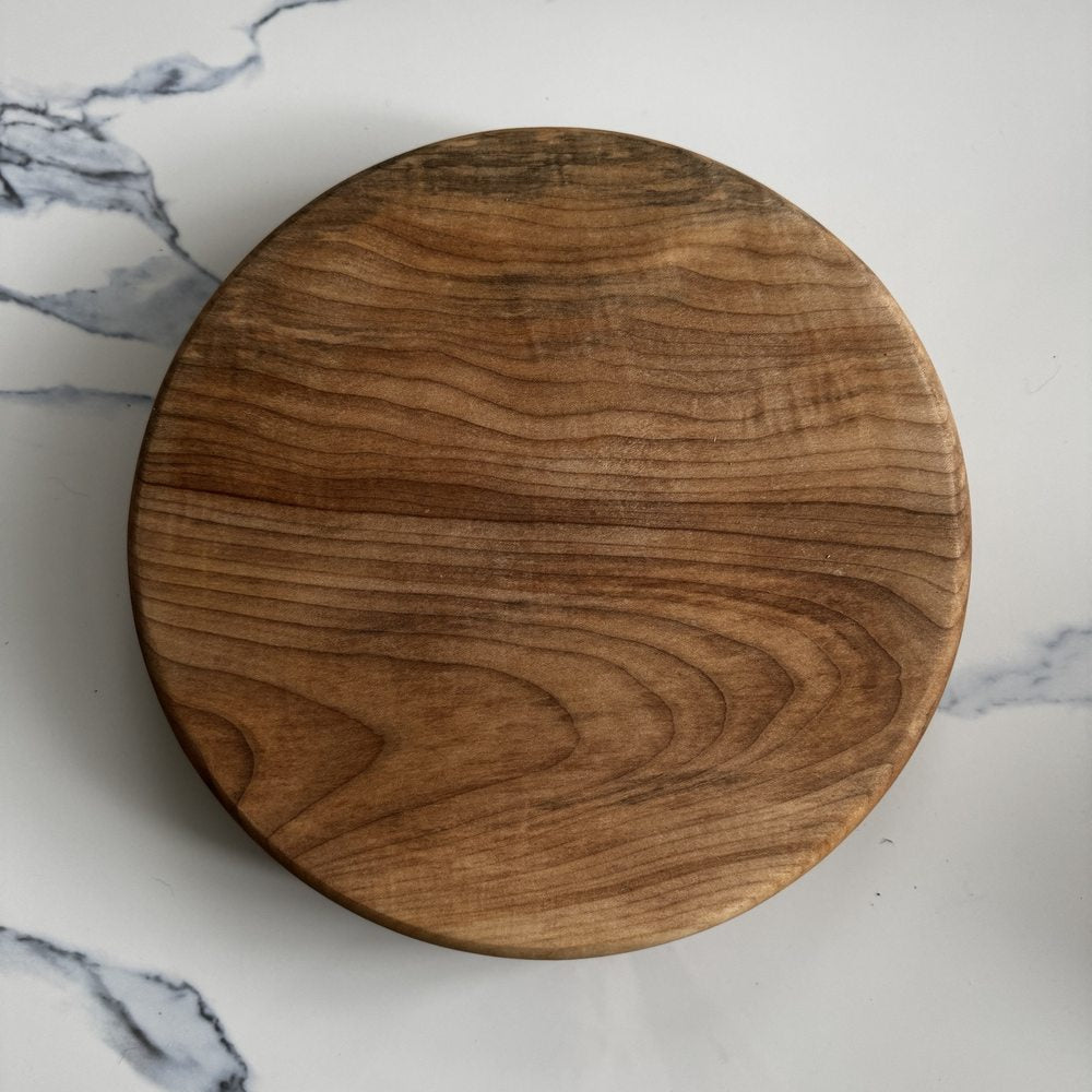 A round wooden cutting board with a rich brown wood grain pattern, photographed from directly above on a white marble surface.