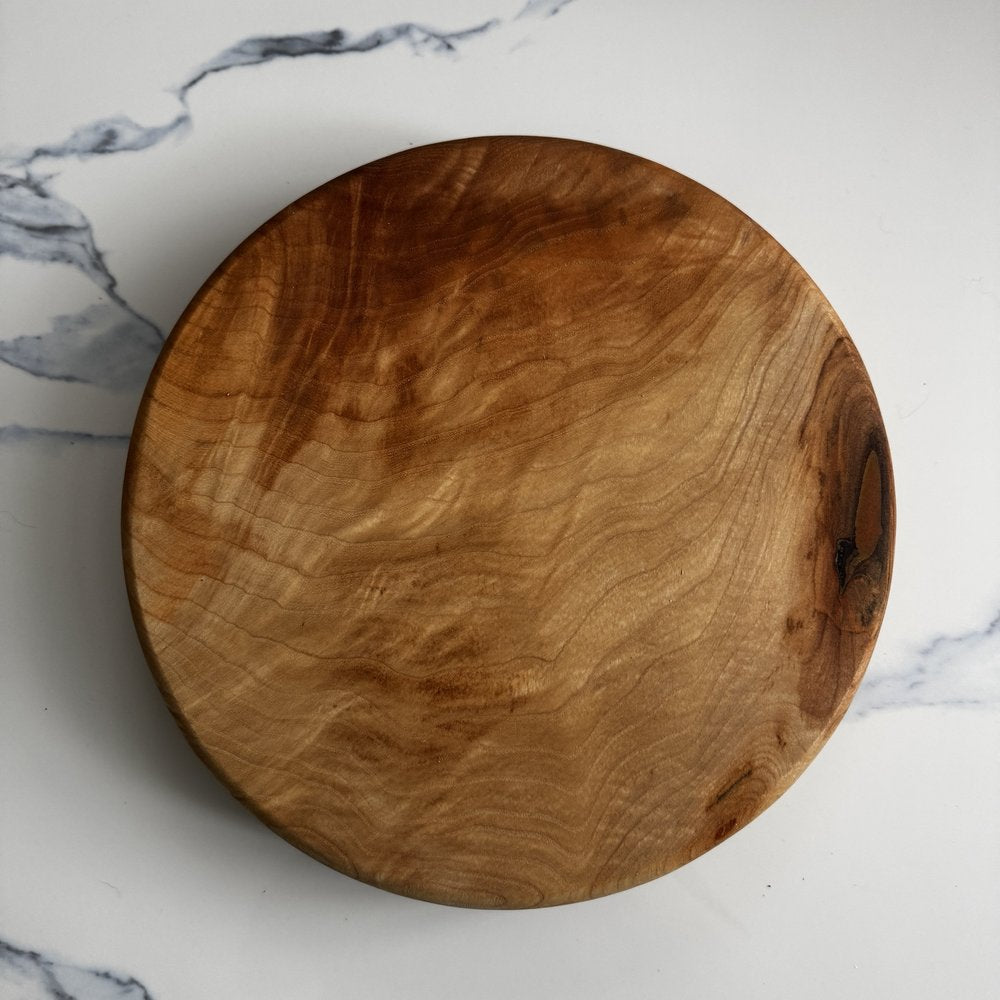 A round wooden serving board with dramatic natural grain patterns, photographed from directly above on a white marble surface.