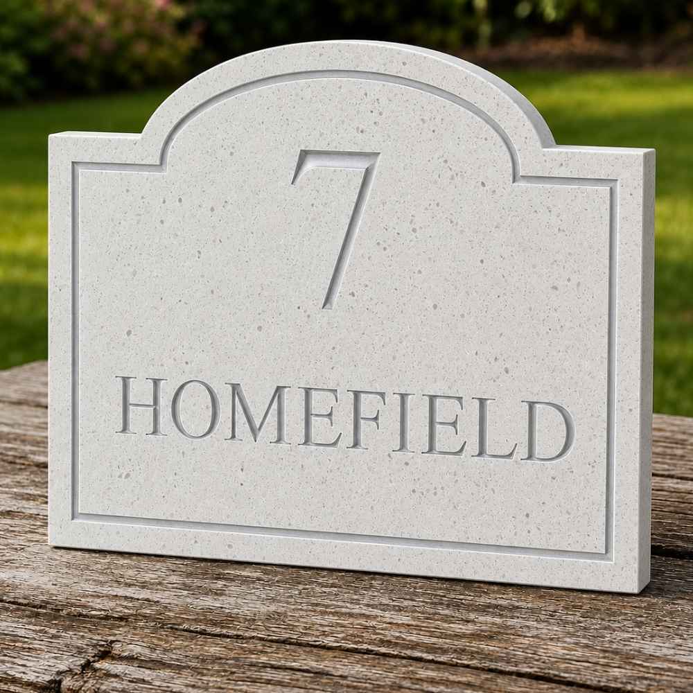 a quartz stone house number plaque reading '7 HOMEFIELD' sits on a weathered wooden surface with a blurred green garden background.
