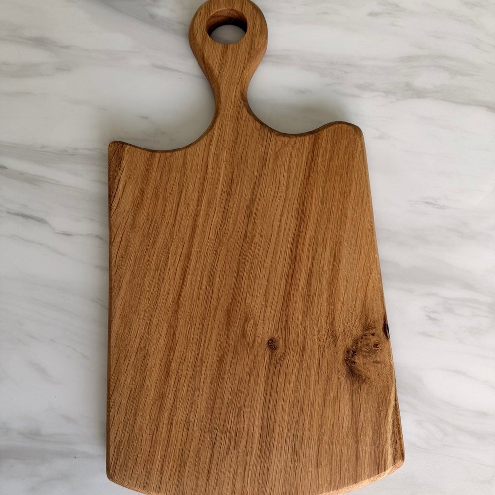 A rectangular wooden cutting board with a rounded handle and a hole in the top, shown on a white marble surface.