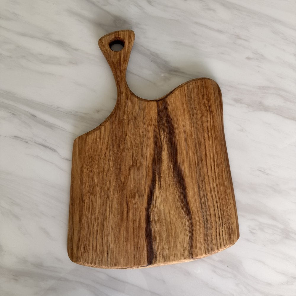 A rustic wooden serving board with a handle and a hole, resting on a white marble surface.