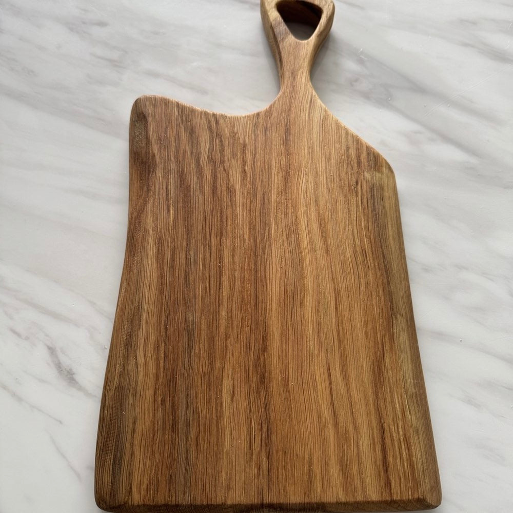 A rectangular wooden serving board with a rounded handle, shown on a white marble surface.