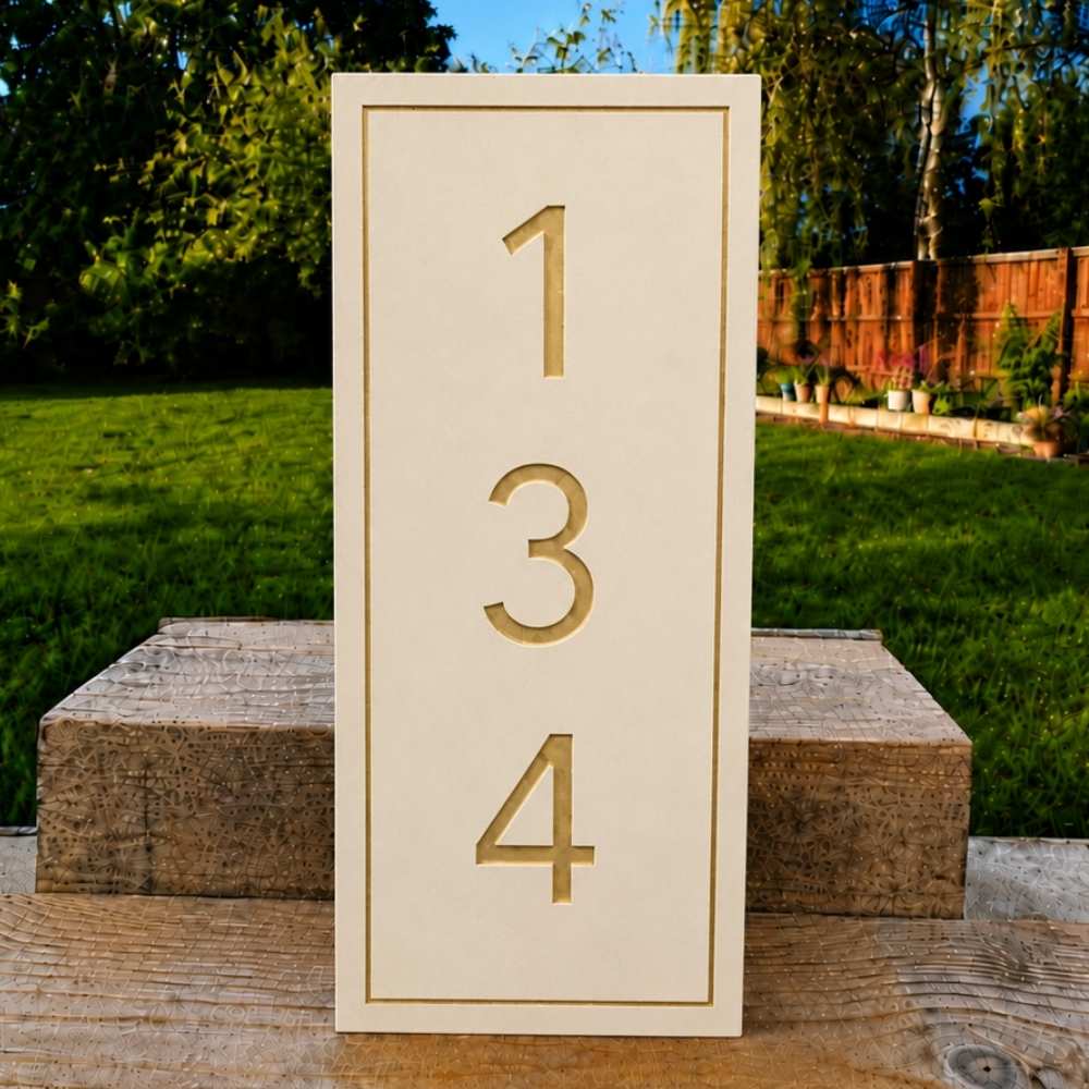 A vertical limestone house number plaque with the numbers 1, 3, and 4 in a matching gold tone, displayed outdoors on a wooden surface with a green lawn and trees in the background.