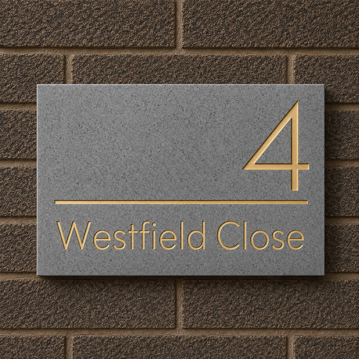 A rectangular granite stone or concrete house number plaque mounted on a brown brick wall. The plaque features a raised gold number 4 and the words 'Westfield Close' in gold lettering.