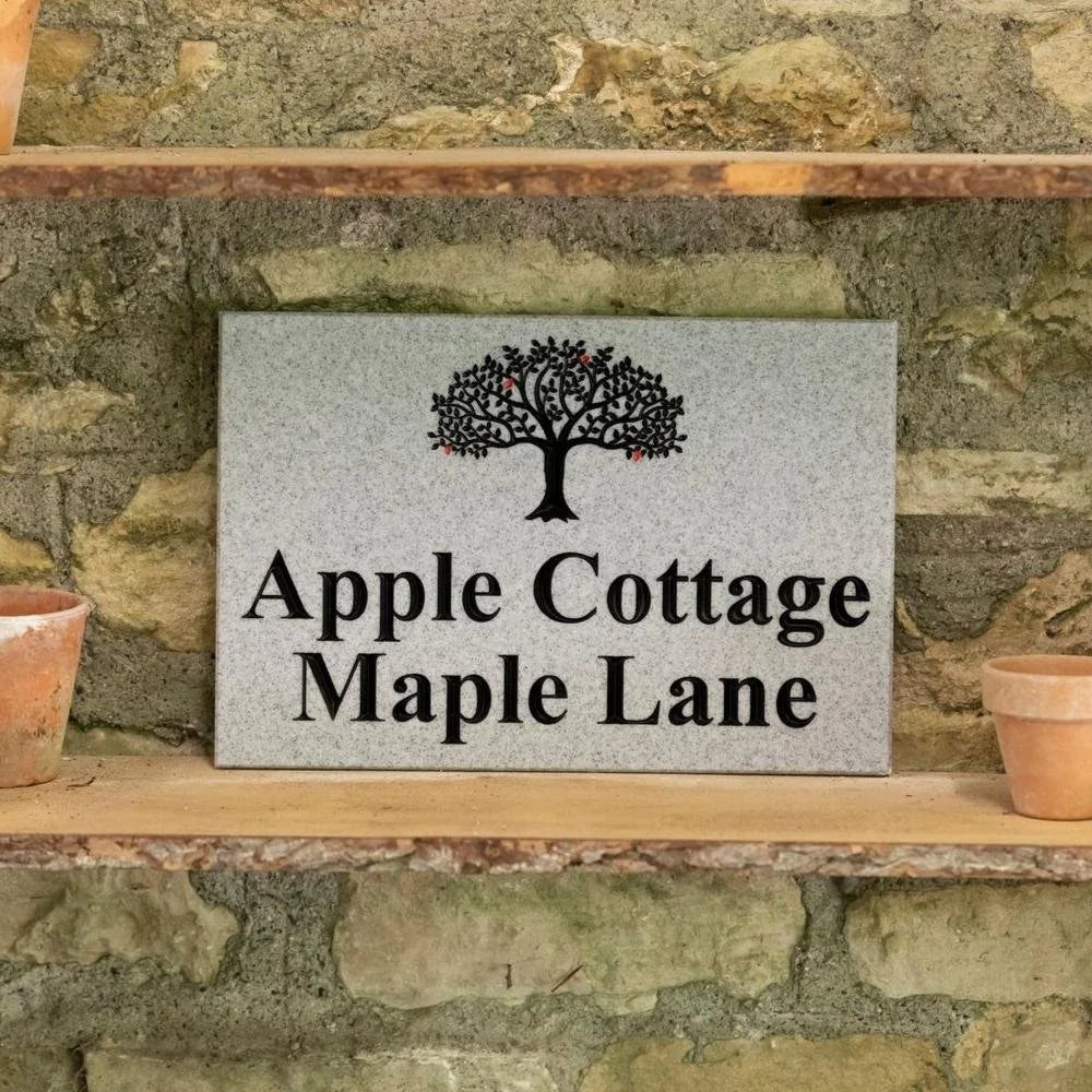 Decorative sign with tree design and text 'Apple Cottage Maple Lane' on a stone shelf.