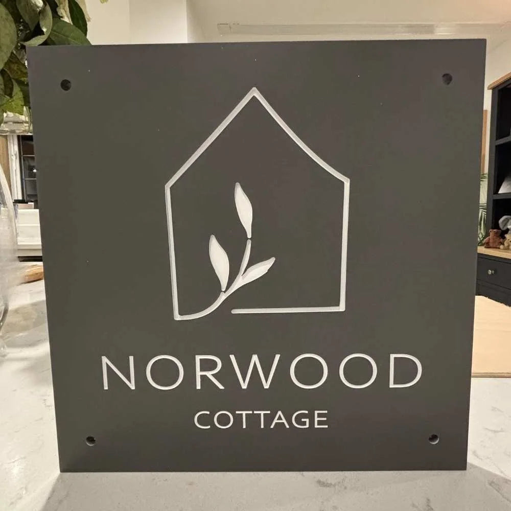 Black sign with white logo and text 'Norwood Cottage' on a marble surface.