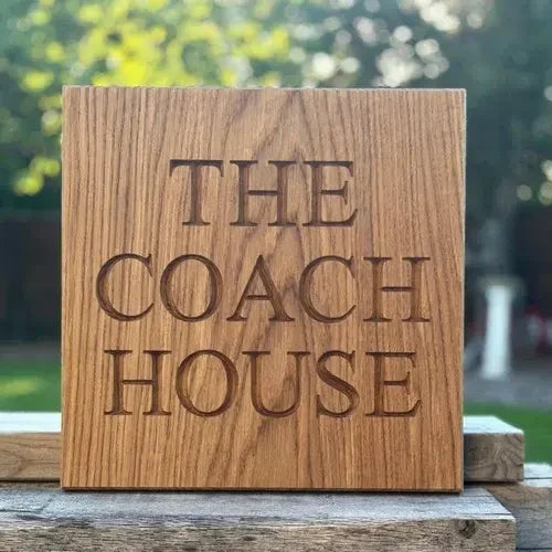 Wooden sign with 'The Coach House' engraved on it, placed outdoors.