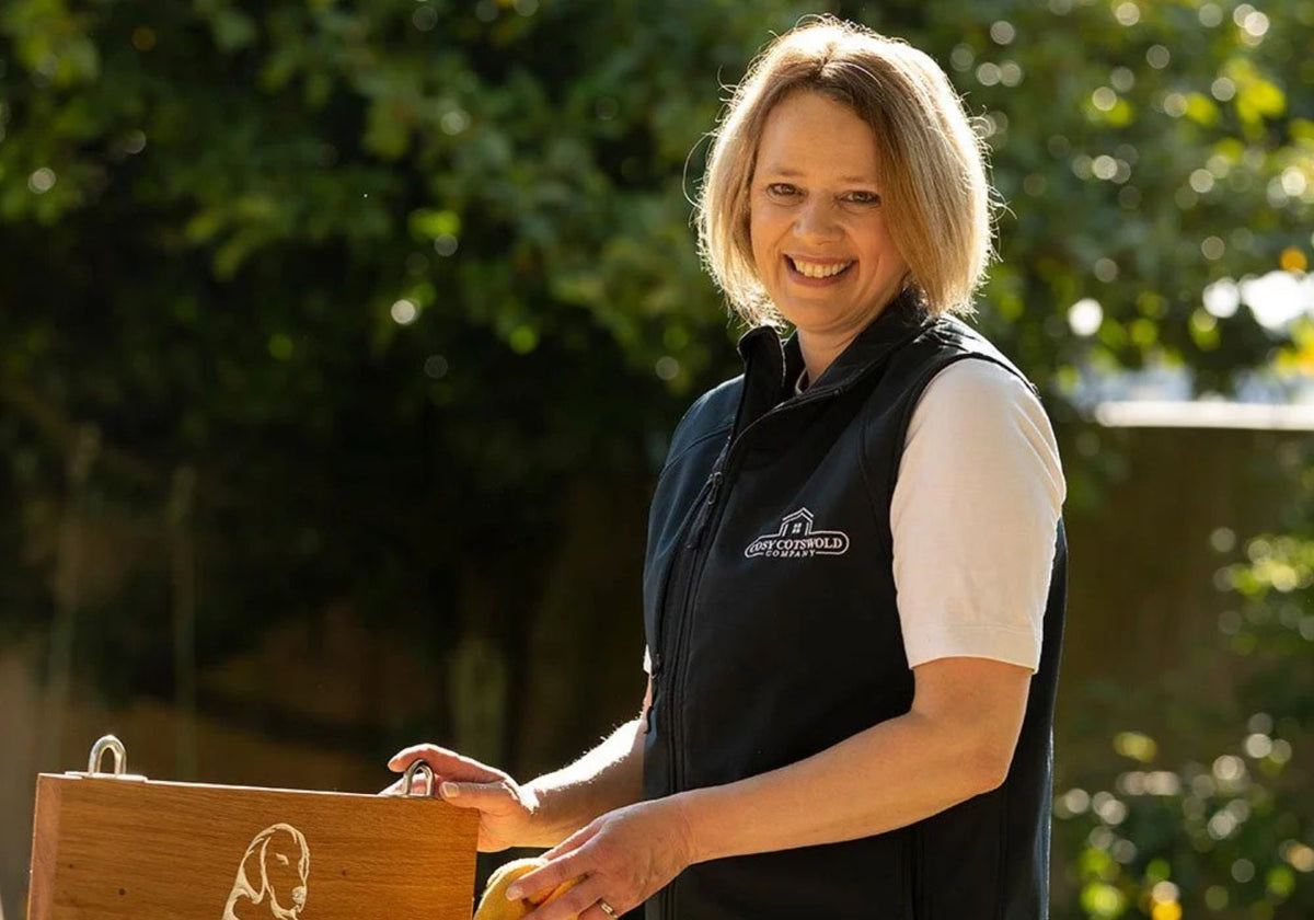 Person wearing a black vest with a logo, standing outdoors with greenery in the background