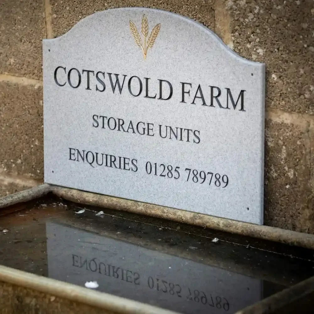Gray sign for Cotswold Farm Storage Units on a brick wall.