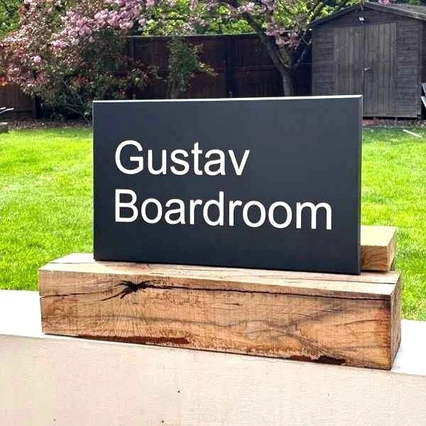Black sign with 'Gustav Boardroom' text on a wooden stand outdoors.