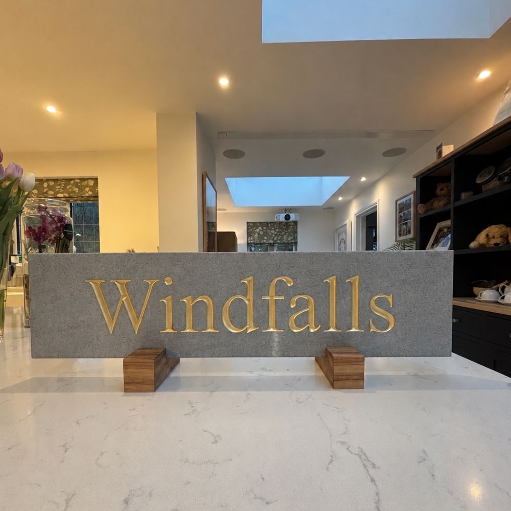 A granite horizontal sign with gold lettering spelling 'Windfalls'.