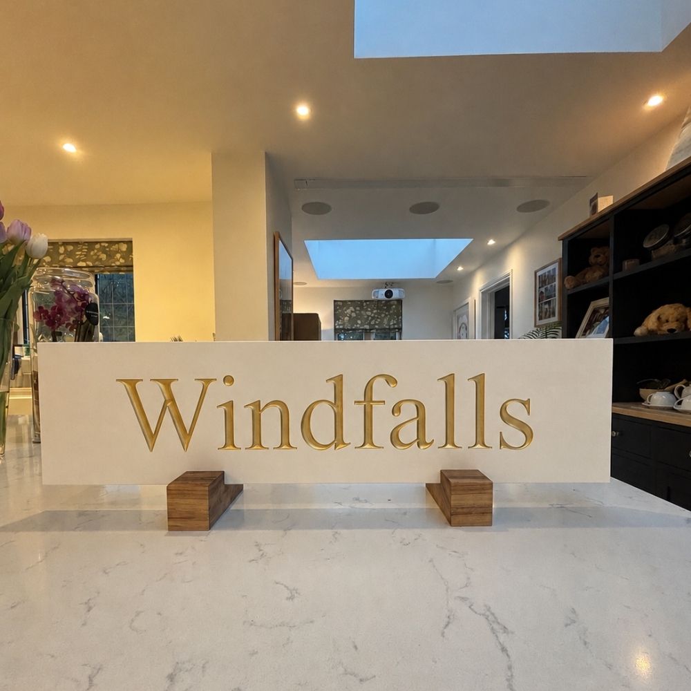 A horizontal limestone plaque featuring the word 'Windfalls' in large gold letters.