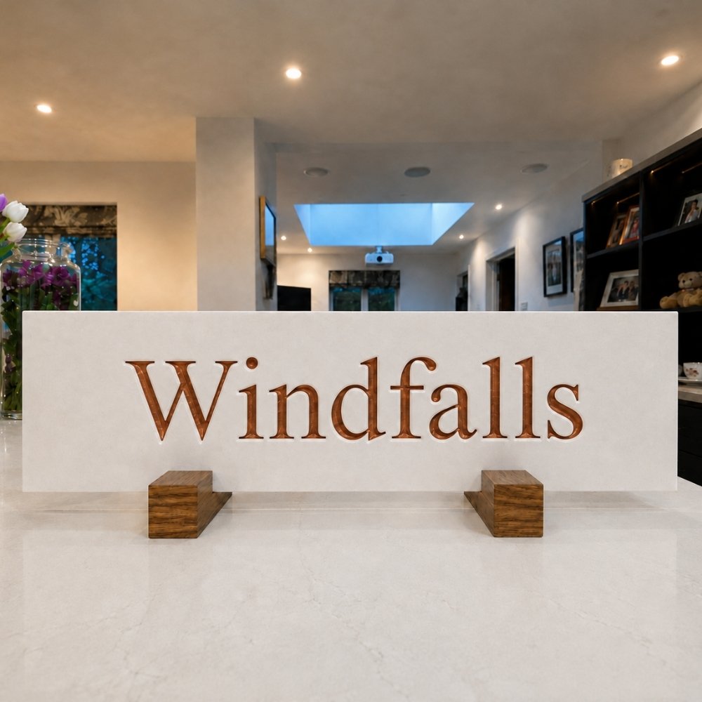 A white horizontal sign with the word 'Windfalls' in Copper font.