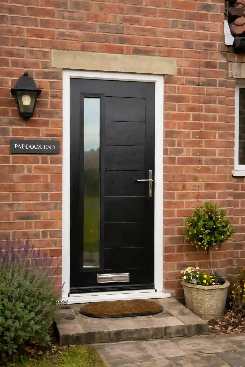 Black door with glass panel on a brick wall with 'Paddock End' sign.