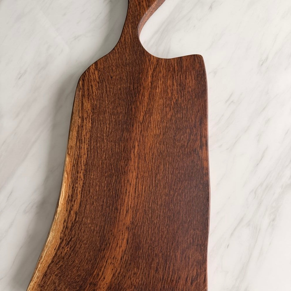 A close-up of a dark brown wooden cutting board with a prominent wood grain texture, resting on a white marble surface.