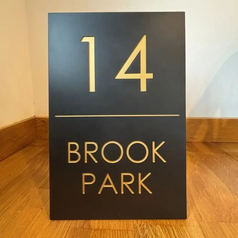 Black sign with gold text '14 Brook Park' on a wooden floor.