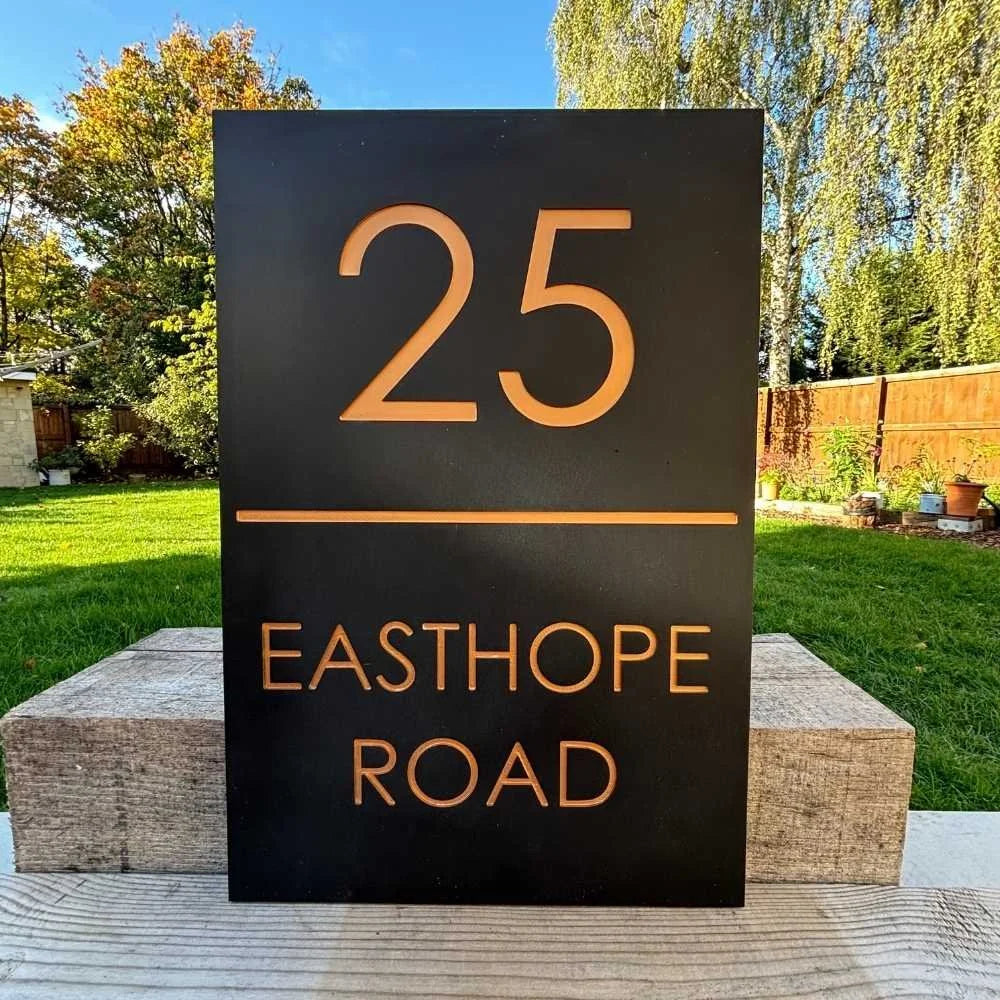 House number sign with '25 Easthope Road' on a black background outdoors.