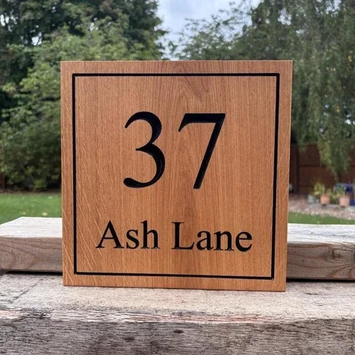 Wooden house number sign with '37 Ash Lane' on a wooden surface with a natural background.