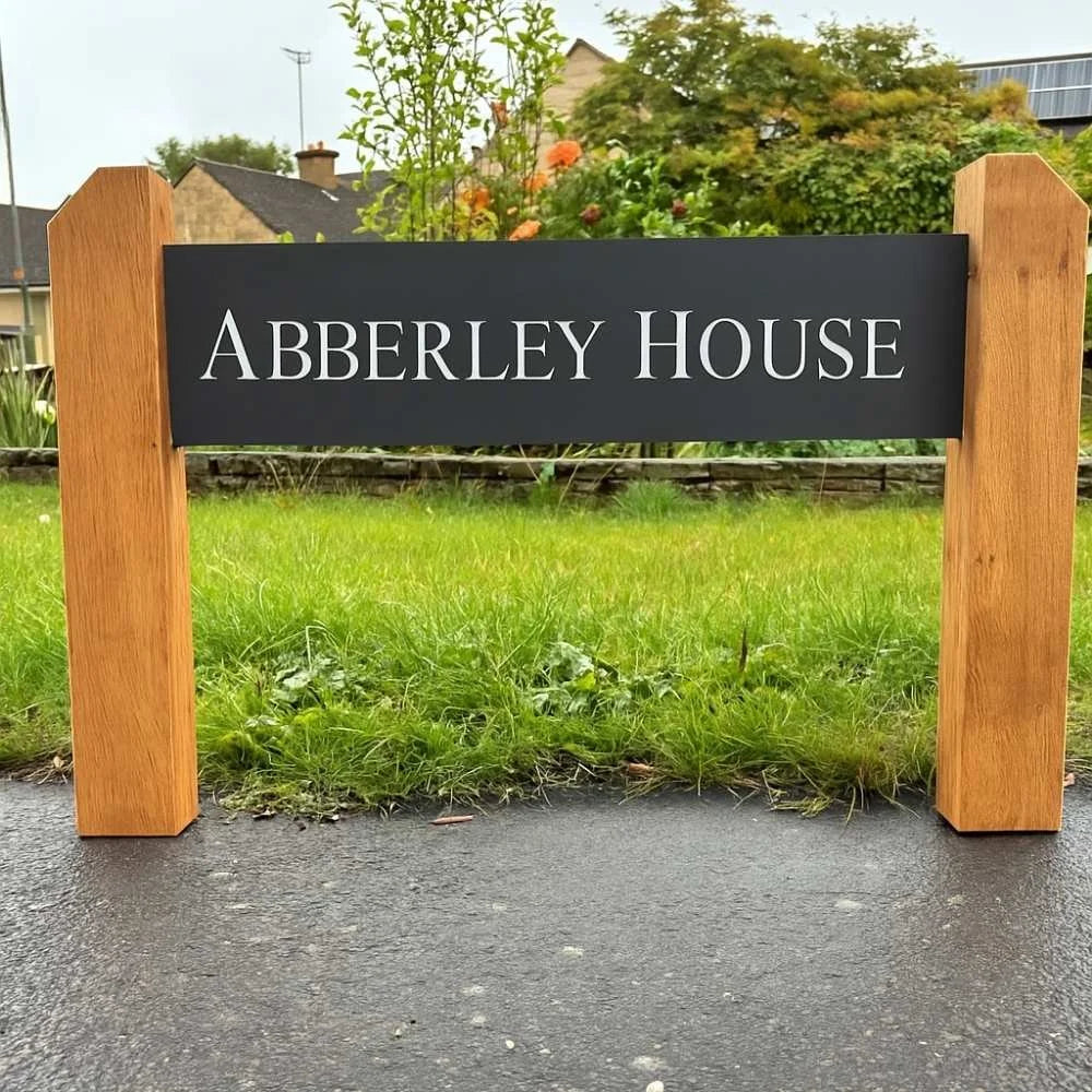 House sign reading 'Abberley House' on a wooden frame with grass and houses in the background.