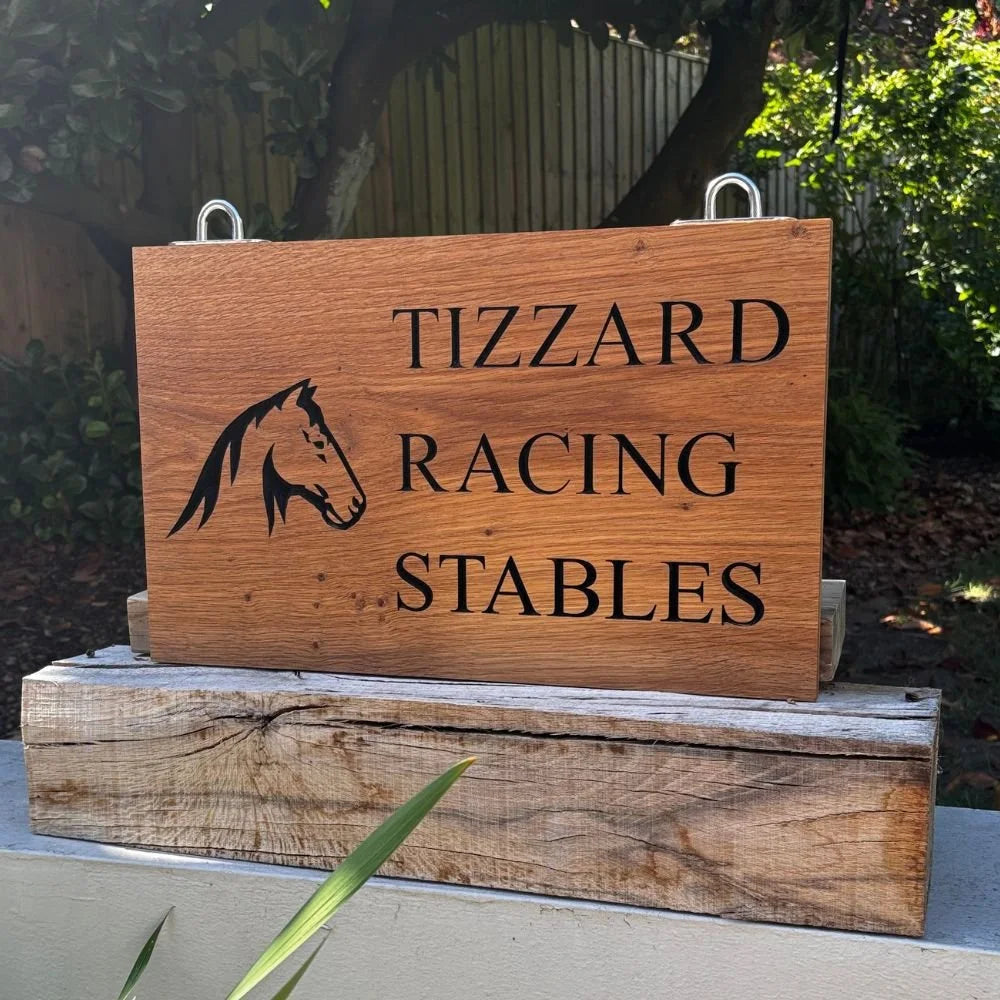 Wooden sign with 'Tizzard Racing Stables' and a horse logo outdoors.