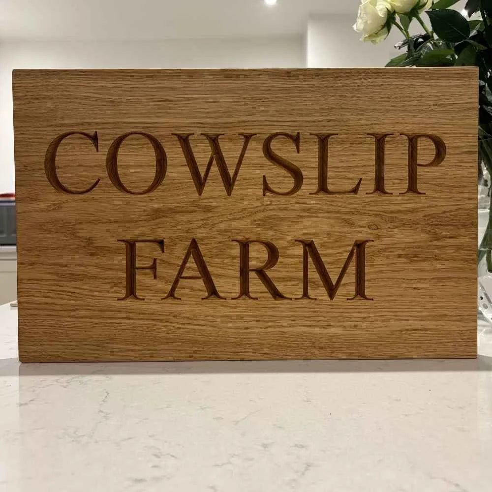 Wooden sign with 'Cowslip Farm' engraved on it, placed indoors.