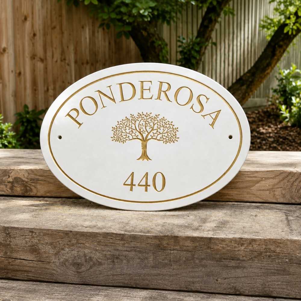An oval white house plaque with gold lettering reading 'PONDEROSA' and '440' around a gold tree emblem, displayed outdoors on rustic wooden steps with a garden fence and plants in the background.