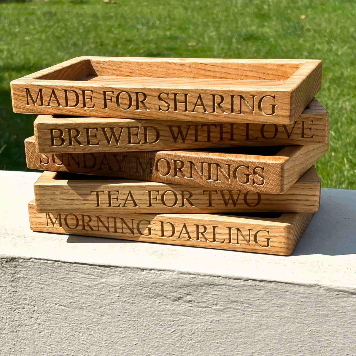 Stack of wooden trays with engraved text on a grassy background