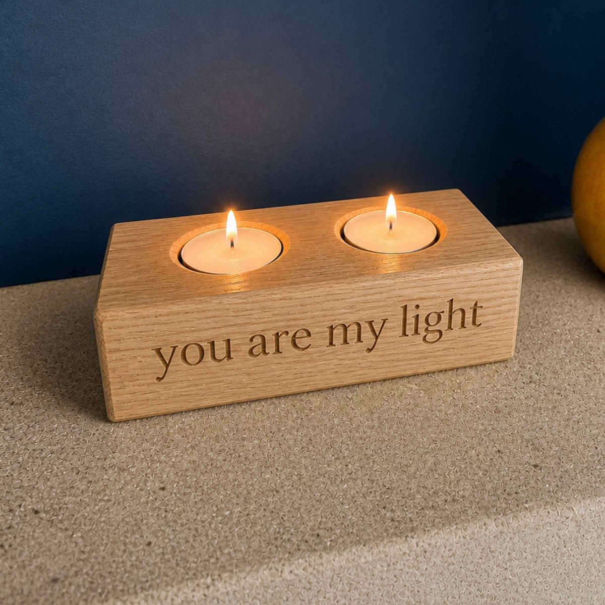 Wooden candle holder with two lit candles and 'you are my light' engraving on a neutral background