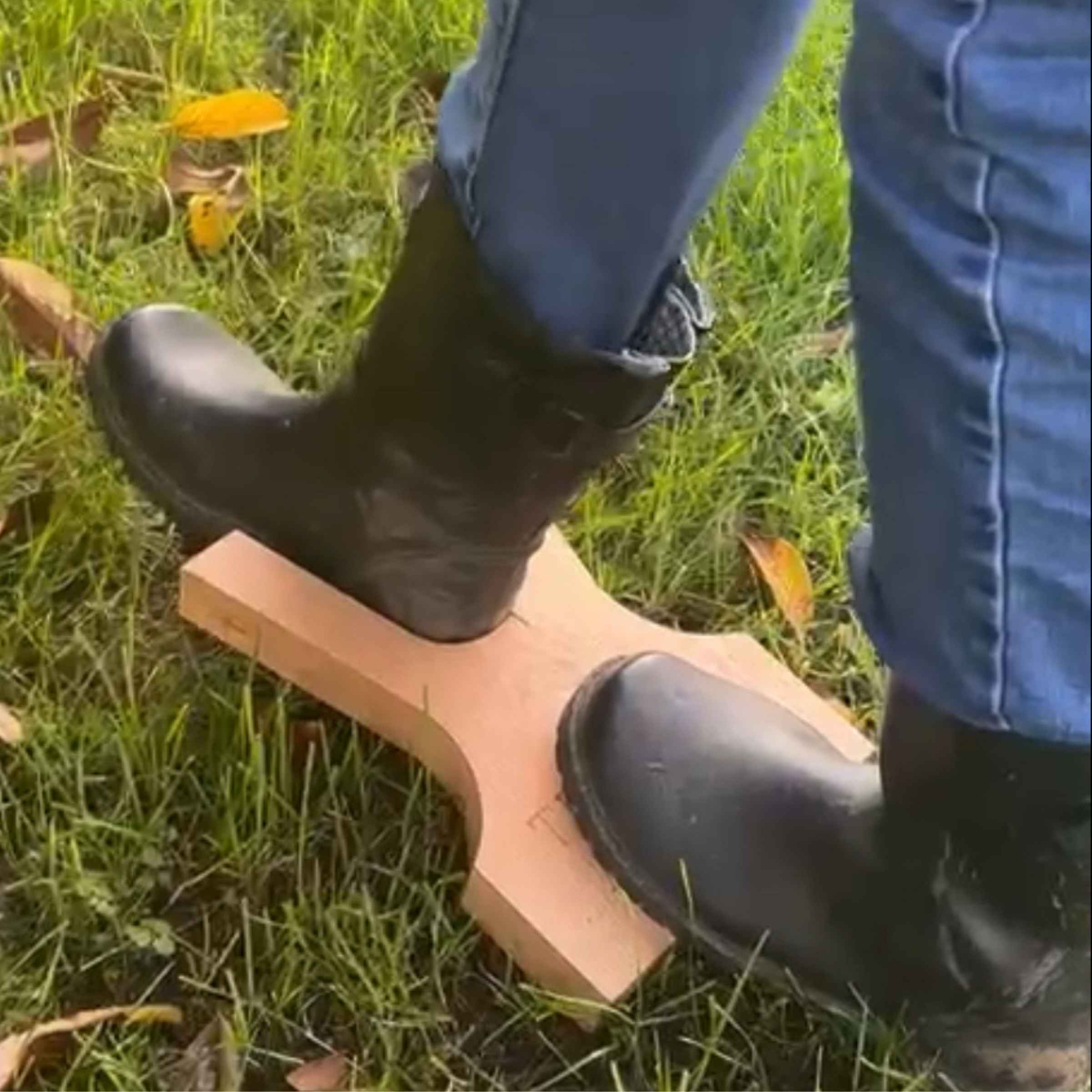 Person wearing black boots stepping onto a wooden block on grass