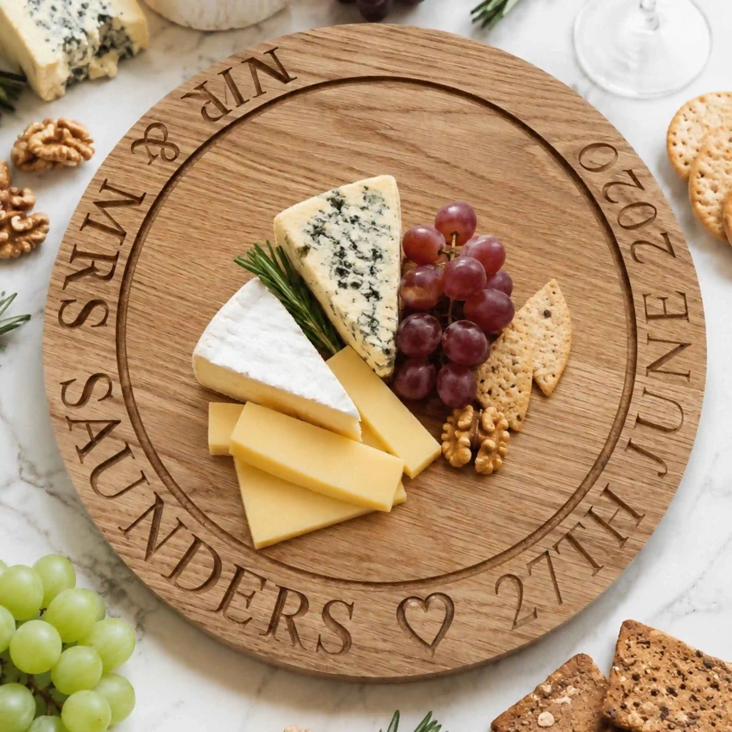 Personalized wooden cheese board with cheese, grapes, and crackers on a marble surface.