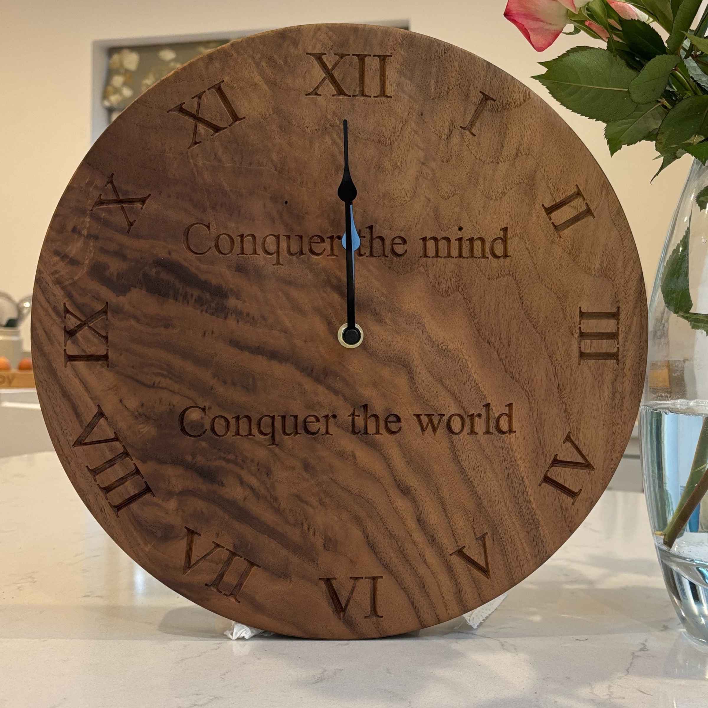 Wooden clock with Roman numerals and motivational text on a surface.