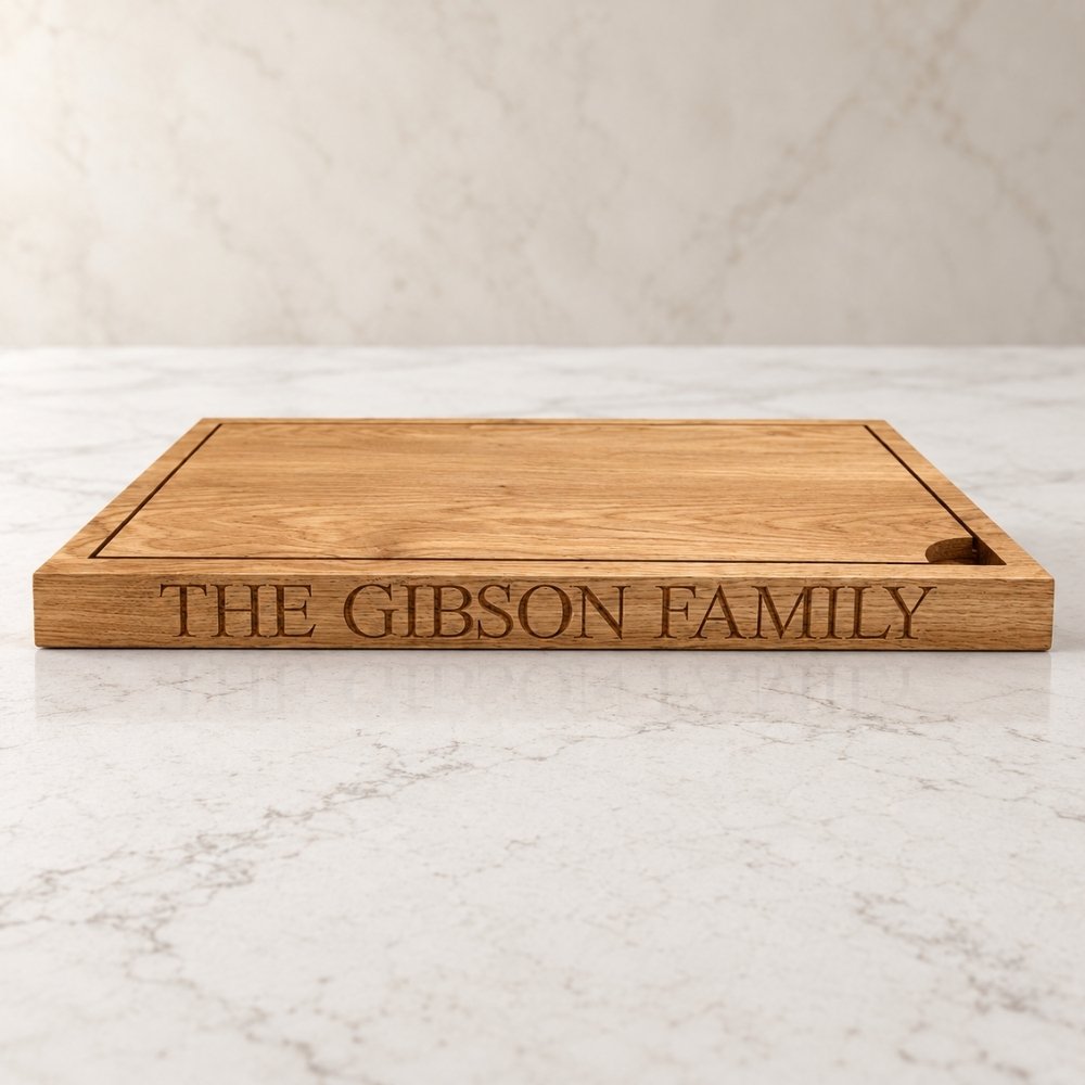 A rectangular wooden serving board engraved with the text 'THE GIBSON FAMILY' on the front, placed on a light marble surface against a matching marble background.